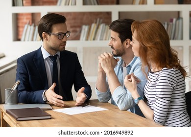 Professional male lawyer financial advisor consulting happy family couple clients in modern office. Interested young customers meeting realtor broker bank worker, discussing agreement or deal.