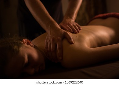 Professional male masseur doing massage for female client at spa salon, studio. Warm romantic illumination, low key