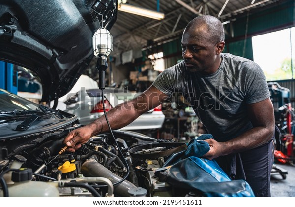 Professional male mechanic measuring the oil
level of the car oil engine in the
garage.