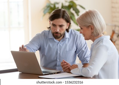 Professional male mentor instructor teaching mature employee help older middle aged worker intern explaining computer software, manager consulting client looking at laptop screen sit at office desk