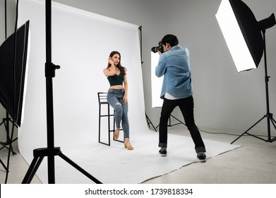 Professional male photographer taking photo of Asian woman in indoor studio with professional set of photographic equipment. - Powered by Shutterstock