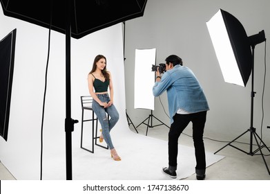 Professional Male Photographer Taking Photo Of Asian Woman In Indoor Studio With Professional St Of Photographic Equipment.