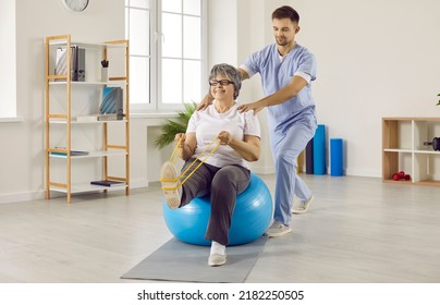 Professional male physiotherapist works with senior female patient in rehabilitation center. Smiling elderly woman sitting on fitness ball in medical office and doing exercises with resistant band. - Powered by Shutterstock