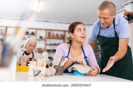 Professional male potter teaches a young woman to create pottery - Powered by Shutterstock