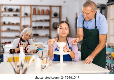 Professional male potter teaches a young woman to create pottery - Powered by Shutterstock