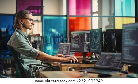 Professional Male Programmer Writing Code on Desktop Computer With Multiple Displays in Stylish Office. Caucasian Man Does Data Scraping For Artificial Intelligence Innovative Technology Start-Up.