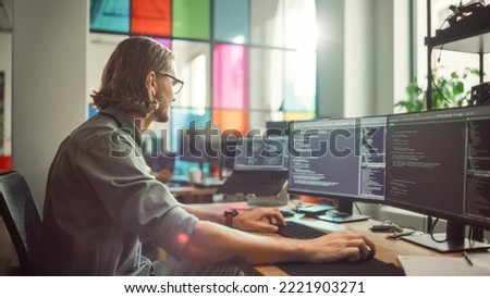 Professional Male Programmer Writing Code on Desktop Computer With Multiple Displays in Stylish Office. Caucasian Man Does Data Scraping For Artificial Intelligence Innovative Start-Up.