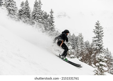professional male skier quickly slides down the snow-covered mountain slope. Fir trees at background. Freeride skiing concept