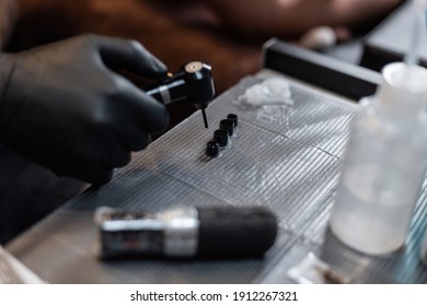 Professional male tattoo artist in black gloves makes ink and mixes paints using a mixer in the studio. Workspace of a tattoo artist. Tattoo preparation process - Powered by Shutterstock