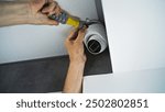 Professional male technician or installer attaches security camera to the ceiling in office building using screwdriver tool. Monitoring and tracking system. CCTV system, video surveillance and privacy