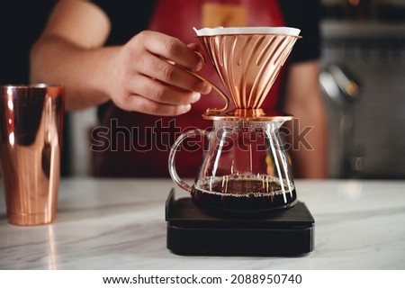 Professional man barista is making drip brewing, filtered coffee, or pour over coffee with hot water and filter paper in coffee shop