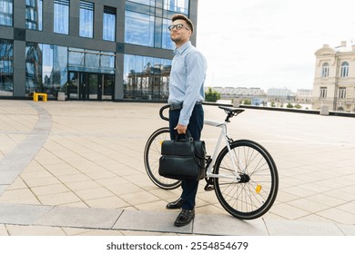 Professional man with a bicycle stands outside modern building holding a briefcase in urban setting - Powered by Shutterstock