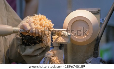 Professional man carpenter using skew chisel for shaping piece of wood on wood turning lathe at workshop - close up side view. Design, carpentry, craftsmanship, manufacturing concept