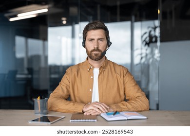 Professional man with headset at office desk using tablet for communication. Focused environment with modern workspace essentials like notebook and pen, embodying multitasking and digital interaction - Powered by Shutterstock