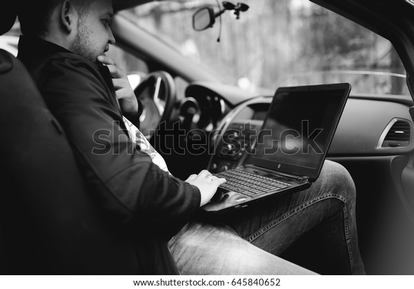 Professional man with a laptop in car tunes tuning\
control system, updating software, gaining access through to\
computer, sitting in\
cabin