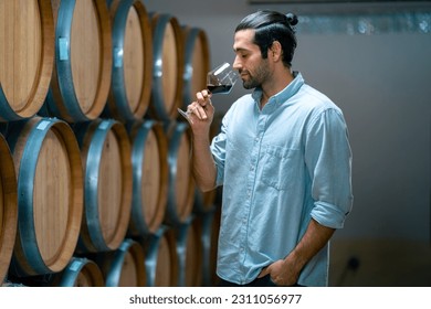 Professional man sommelier testing red wine in wine glass with tasting and smelling at wine cellar with wooden barrel in wine factory. Winery liquor manufacturing industry and winemaker concept. - Powered by Shutterstock