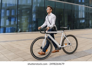 A professional man walks his bicycle beside a modern glass office building, exuding confidence and style.

 - Powered by Shutterstock