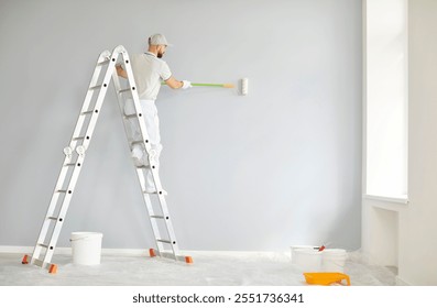 Professional man, working as a painter or builder, uses a roller brush to paint walls during a renovation project. Equipped with a ladder, he brings expertise to the construction and transformation.