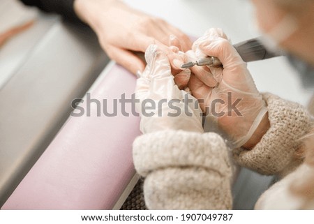 Professional manicure master is doing nails for happy client in beauty salon