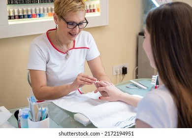 Professional Manicurist Removing Polish From Female Client's Nails With Cotton Pad At Table In Nail Salon