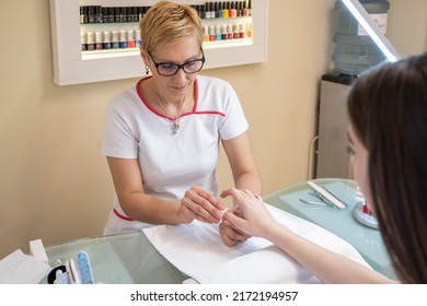 Professional Manicurist Removing Polish From Female Client's Nails With Cotton Pad At Table At Workplace In Nail Salon