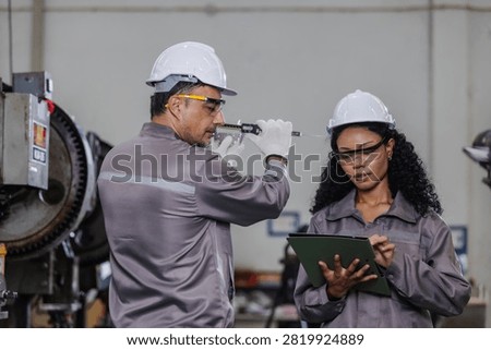 Professional manufacturing engineers performing precision quality inspection while recording measurement data on a digital tablet in a modern industrial factory. 