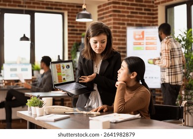 Professional marketer using the internet to display advertising strategies, analyzing client data in modern workspace. Two female coworkers concentrating on business analytics on laptop.
