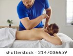 Professional massagist specialist at health center, spa studio, parlor uses elbow for therapeutic remedial shiatsu or Lomi technique spine back massage to help beautiful woman lying on table bed couch