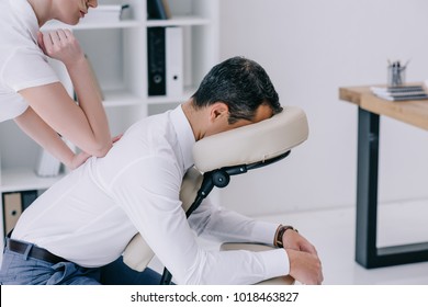 professional masseuse doing seated back massage for businessman at office