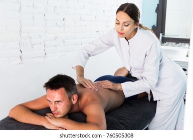 Professional Masseuse Performing Back Massage To Positive Swedish Male Client In Spa Center
