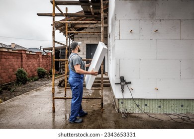 Professional master holds adhesive styrofoam to the wall. Building insulation saves energy. Facade master. Industrial theme - Shutterstock ID 2343653331