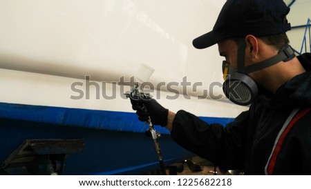 Professional master man in a robe and puller with spray gun puts a layer of paint or ceramics on the yacht. Concept of: Dangerous work, Chemistry, Paints, Garage, Transport Service.
