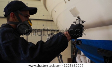 Professional master man in a robe and puller with spray gun puts a layer of paint or ceramics on the yacht. Concept of: Dangerous work, Chemistry, Paints, Garage, Transport Service.