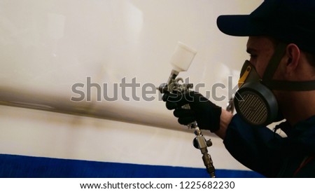 Professional master man in a robe and puller with spray gun puts a layer of paint or ceramics on the yacht. Concept of: Dangerous work, Chemistry, Paints, Garage, Transport Service.