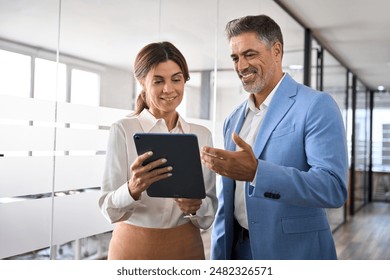 Professional mature business people, two happy middle aged business man and woman executives partners team working together checking corporate results collaborating standing in company office. - Powered by Shutterstock