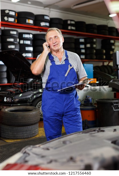 Professional mature mechanic in\
auto repair shop making order on phone for necessary spare\
parts