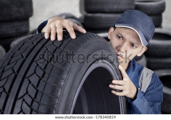 Professional mechanic checking car tyre while\
looking at texture of tyre in his workshop\
