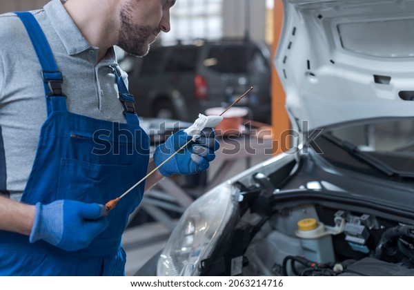 Professional mechanic\
doing a vehicle inspection, he is checking a car\'s oil level and\
quality using a\
dipstick
