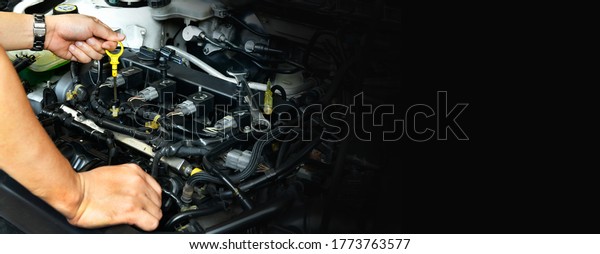 A professional mechanic is holding the oil\
dipstick check the oil level in car engine on black background free\
space on right side for text.