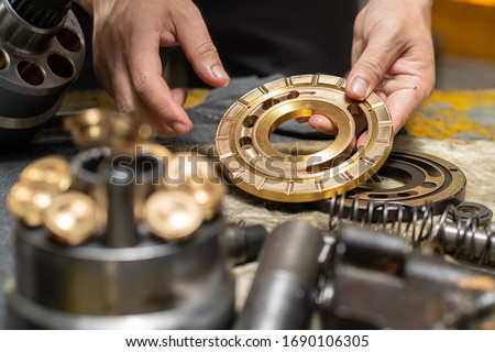 Professional mechanic man holding Valve plate of the hydraulic piston pump to inspection and repair maintenance heavy machinery 