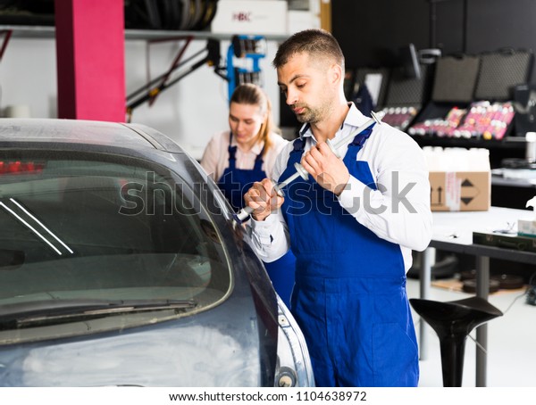 Professional mechanic performing dent repair on\
car body before painting in auto\
workshop