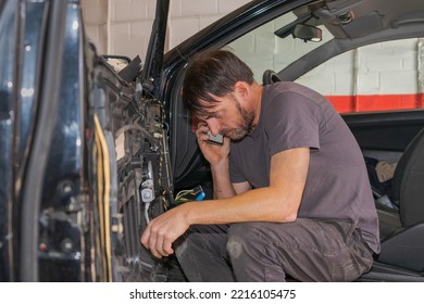 The Professional Mechanic, Sitting In The Car With The Door Open, Calls The Owner Of The Car On His Smartphone And Explains That He Is Repairing The Inside Of The Door In His Workshop In Granada.