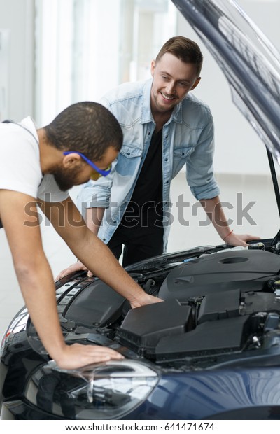 Professional mechanic talking to a car owner\
while examining his car positivity communication help service\
automotive engine motor annual checkup professionalism support\
advising people\
technology