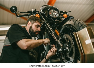 A professional mechanic unscrews the front wheel of a motorcycle. Bike is on the lift at the service station.