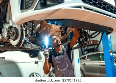 Professional mechanic using flashlight, examining underside of lifted vehicle in well equipped car workshop