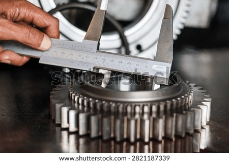 Professional mechanic using a vernier caliper tool to check exact dimensions and size of a steel gear component in an automotive workshop.