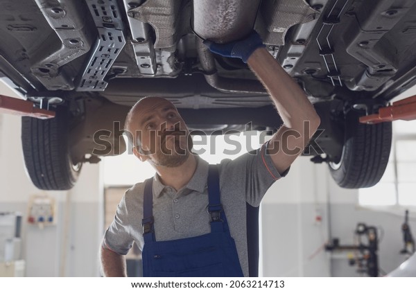 Professional mechanic working under a car\
in a repair shop, car maintenance and repair\
concept