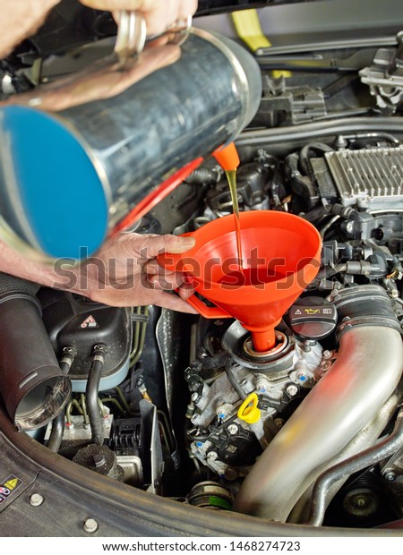 a professional\
mechanical employee of a car service workshop make a oil change at\
the open bonnet motor engine