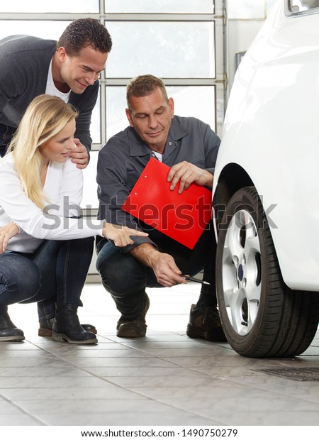 a professional mechanical employee of a car\
service workshop and tire service squads with a pair of a men and a\
blonde women at the car and check the tires. a good service and\
consulting in the garage