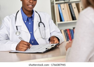 Professional medic female african doctor consult sick woman patient writing information filling medical registration form paper at appointment at visit in clinic. Medicine women healthcare, close up